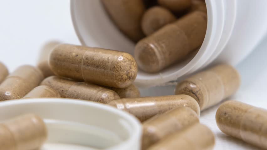 A closeup of Herbal medicine capsules spilling from a white bottle onto a white surface