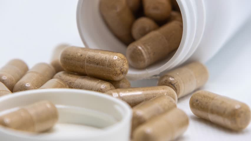 A closeup of Herbal medicine capsules spilling from a white bottle onto a white surface