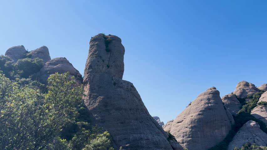 Walking in the mountains of Montserrat in Spain in summer. Panorama of mountain peaks and green plants against the blue sky. Trails for active recreation