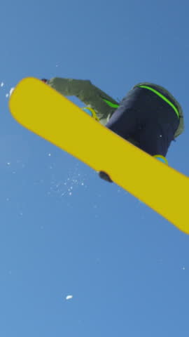 SLOW MOTION: Extreme snowboarder man riding in sunny mountain snow park and jumping over big air kicker in sunny winter. Young pro snowboarder jumping over the sun