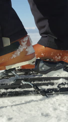 SLOW MOTION SLOW MOTION CLOSE UP: Skier stepping into the ski bindings with his ski boots on a sunny morning. Located at modern European ski resort in the Alps with chairlift in the background