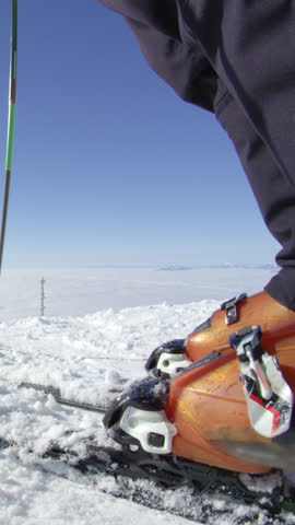 SLOW MOTION CLOSE UP: Skier removing fresh snow from skis on a top of the mountain above fog at European ski resort in the Alps on a sunny perfect cold and cloudless winter day with no people