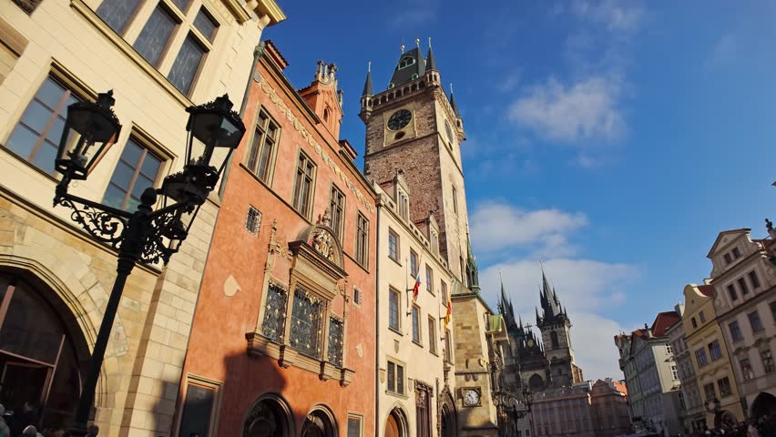 View of historical buildings with the tall clock tower of the Prague town hall in the city center under a clear blue sky.