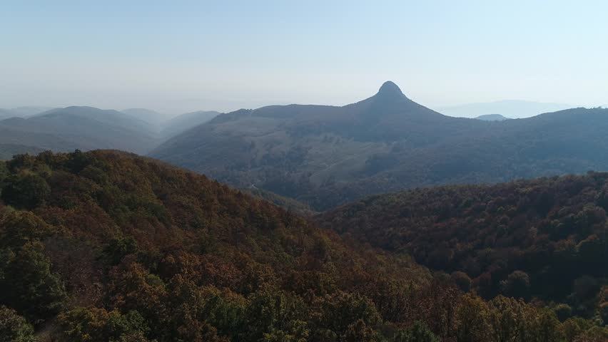 Interesting shaped mountain on the horizon surrounded by hills in fall as trees are changing color.