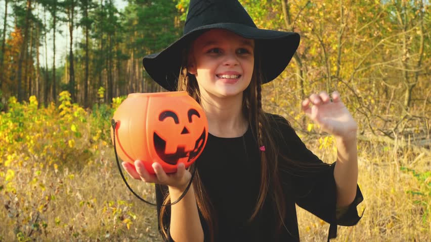 Halloween girl in a witch costume. Trick or treat. A child an carnival on autumn forest. Celebrate Halloween. Girl in the forest smiles and holds a basket of sweets