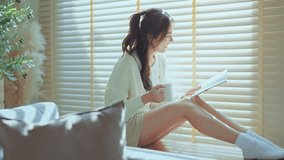 Happy asian woman drinking coffee or tea while reading a book in front of window relaxing in her living room at home, Lifestyle home concept. - Powered by Shutterstock - Get 15% off with code: PIKWIZARD15
