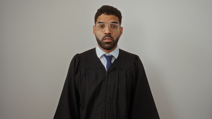 Judge gown-clad young hispanic man standing with mouth shut as if zipped by finger, silent and serious over isolated white background