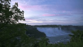  Early evening view of Niagara Falls surrounded by lush green trees, with pink and purple hues painting the sky, showcasing the serene beauty of the natural landscape. - Powered by Shutterstock - Get 15% off with code: PIKWIZARD15