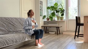 Calm woman sitting on sofa deep breathing during meditation at home. Self-help of middle aged female stress relief in daily routine reset mind with eyes closed, placing hands on chest, abdomen. - Powered by Shutterstock - Get 15% off with code: PIKWIZARD15