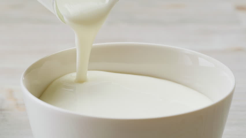 Pouring kefir yogurt into glass cup close-up. Glass with kefir or milk, lactic acid product dairy products concept. Drinking fresh lactose free in morning.
