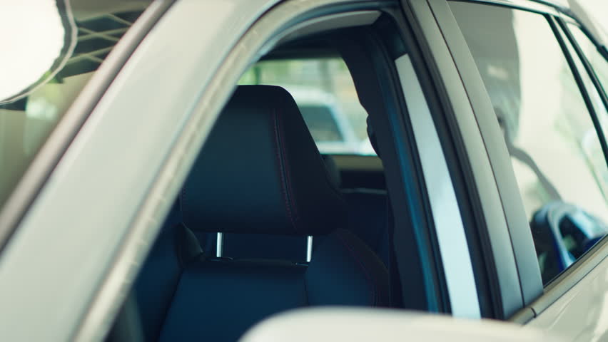Exterior detail close up of steel white car body door post, windows, and driver chair inside. Panning shot of parked vehicle and leather black seat in automobile interior