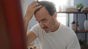 Man looking at mirror in spa room adjusting hair while wearing casual white shirt in serene indoor wellness setting surrounded by soft lighting and decorative elements. - Powered by Shutterstock - Get 15% off with code: PIKWIZARD15