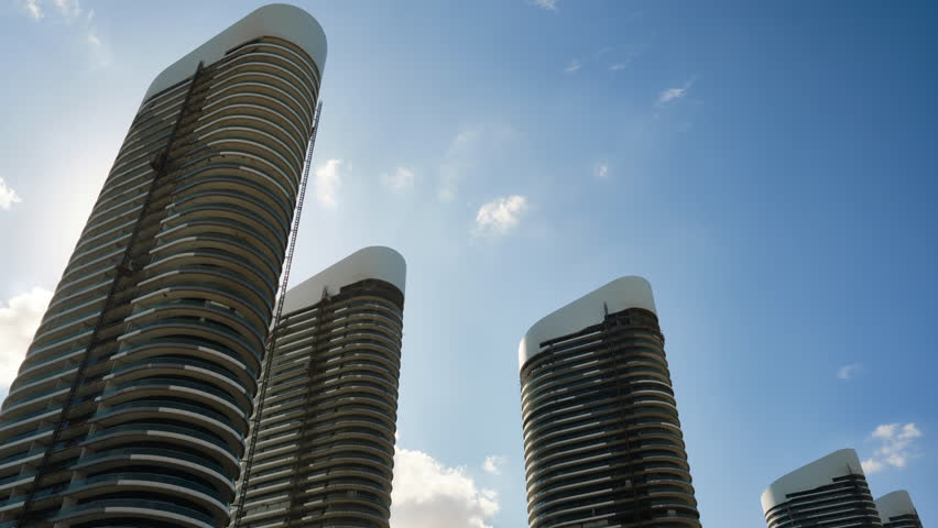 Low angle view of high rise office buildings under construction and clouds passing by at daytime. Skyscrapers timelapse. Tall corporate buildings at New Alamein, Marsa Matrouh governorate, Egypt