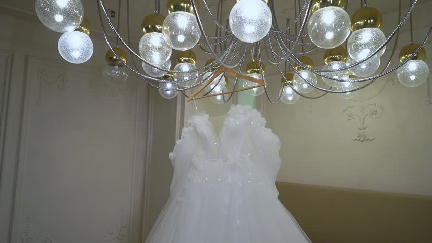 A stunning white wedding dress is showcased in a modern room with a glamorous chandelier and elegant decor, ideal for a bridetobe looking for sophistication and luxury for her special day