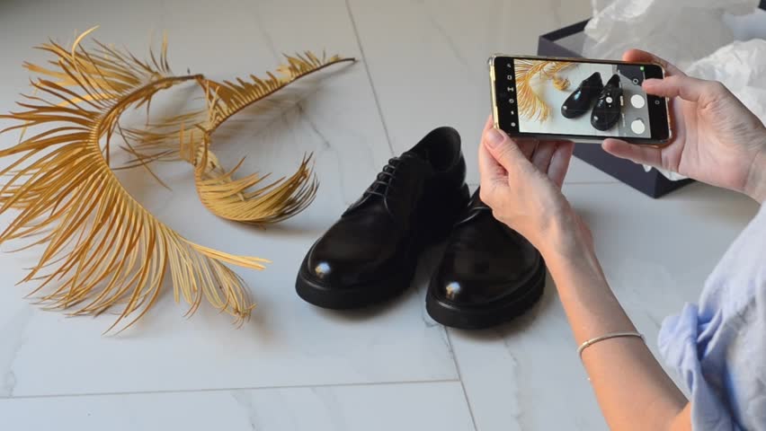 Woman takes photo of men shoes on smartphone for online sale. Smart use. Second life of unnecessary things. Caring for nature. Second hands, second life of things. Online store for selling used items.