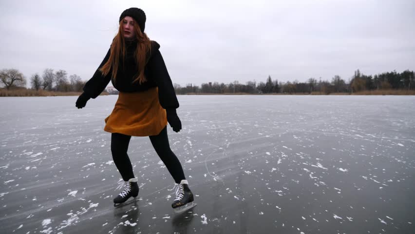 Young sportswoman shod in figure skates sliding on ice river at winter. Female skater practicing skills at lake on frozen day. Girl enjoying sport and having active leisure at cold weather. Slow mo