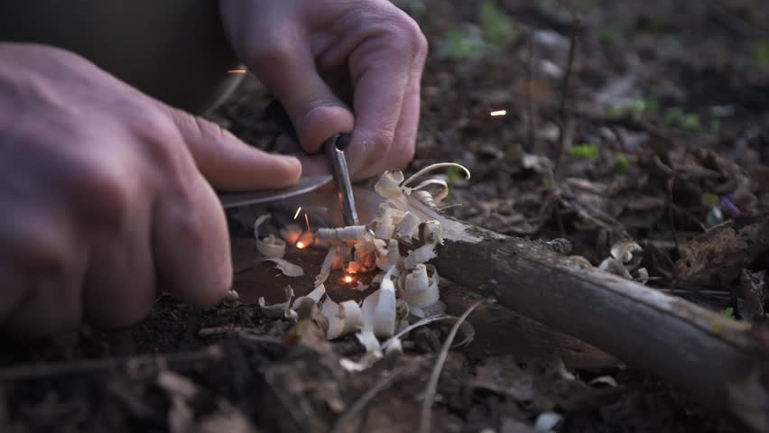 A man ignites fire using a knife and firestarter, creating sparks over wood shavings. This close-up captures the essence of survival skills and outdoor bushcraft