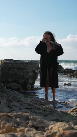 Woman Beach Coat Ocean: A woman wearing a black coat walks on the beach near the ocean.