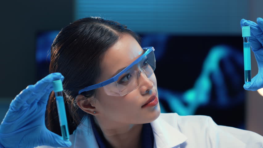 Scientist wearing a lab coat and protective glasses is carefully examining a test tube containing a blue liquid - Powered by Shutterstock - Get 15% off with code: PIKWIZARD15