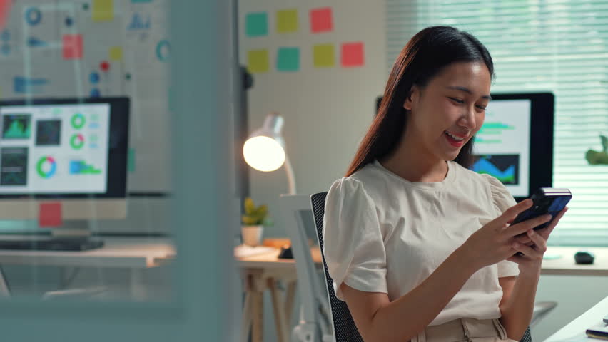 Cheerful atmosphere surrounds an asian office worker enjoying her smartphone during a break, smiling and relaxing - Powered by Shutterstock - Get 15% off with code: PIKWIZARD15