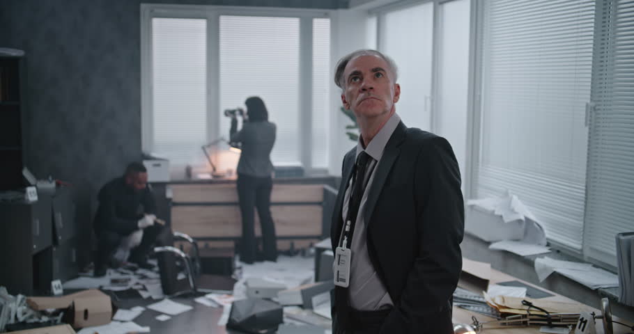 Office robbery case: Medium close up of male detective examining crime scene. Female criminalist takes photos of clues and evidence, African American policeman looks for fingerprints in the background