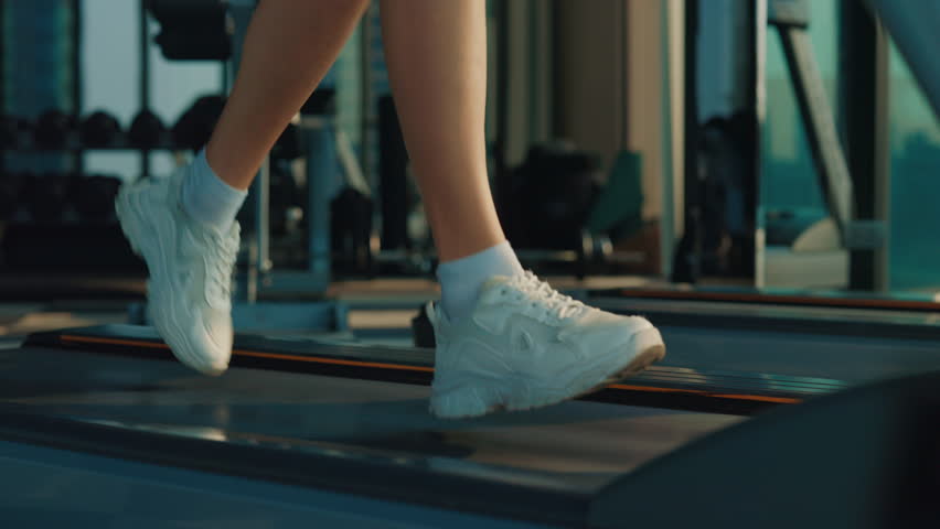 Close Up of Female Person's Feet Running on a Treadmill in a Gym. Jogging. Healthy Lifestyle. Woman in professional sneakers runs on treadmill at gym closeup