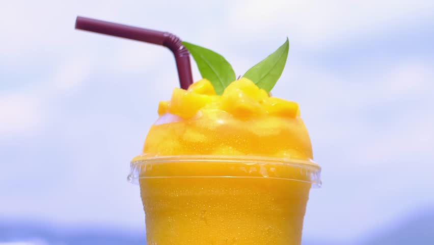 Smoothie made from fresh mango fruits against the backdrop of a seascape. Fruit and yoghurt ice cream decorated with leaves. Glass of tropical dessert close-up.