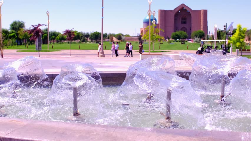 Fountain against the background of the Mausoleum of Khoja Ahmed Yasawi. Jets of water from a fountain rise in a beautiful pattern on the street of the city of Turkestan.