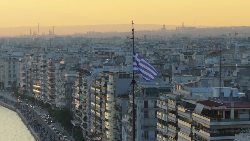 Greek flag with Nikis Avenue, traffic and people in the background in Thessaloniki, Greece