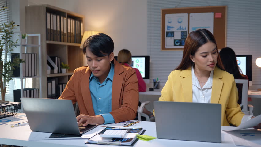 Two business professionals collaborating on a project, analyzing data and strategizing on laptops in a brightly lit office