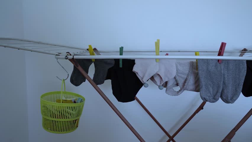 Homemade clothesline with hanging basket for clothespins and various items of laundry hung out to dry.
