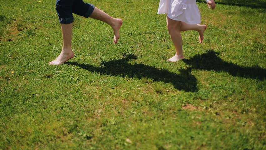 A couple in love and a girl running through the green grass on a sunny day, the camera shoots their legs in slow motion