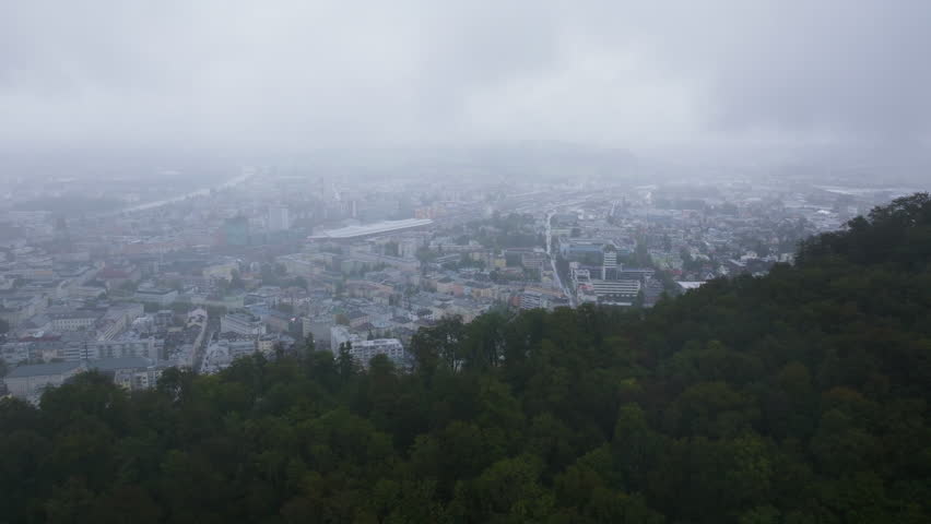 Aerial view of Salzburg, Austria, partially covered by low clouds. The Salzach River is flowing through the city on a cloudy day