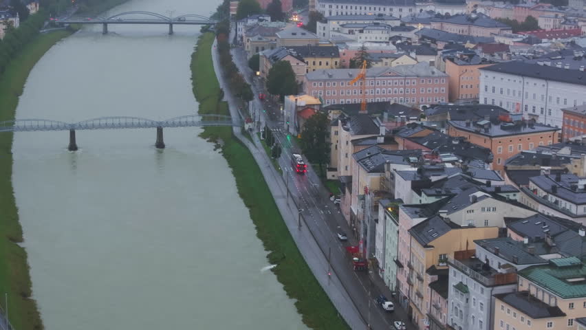 Aerial views highlight Salzburg historic center, with the Salzach River flowing elegantly beneath a cloudy sky, showcasing the city