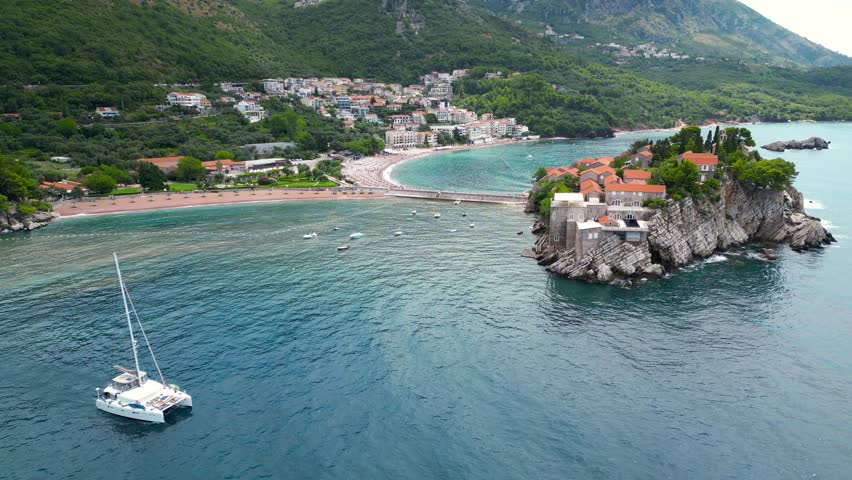 Aerial landscape of Sveti Stefan, Montenegro. Tourist boat passing. Famous and luxury travel destination. Static footage.