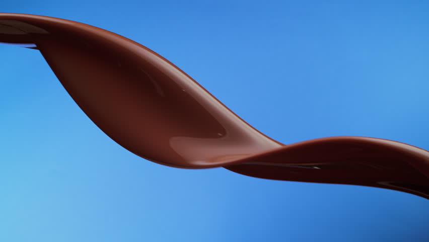 A ribbon of viscous chocolate liquid flowing in slow motion on blue background