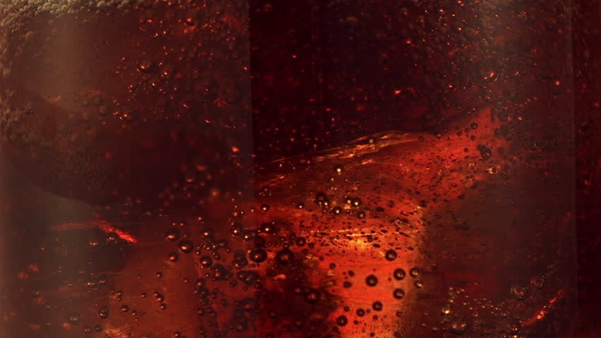 full screen view of ice tea or apple juice pouring inside a glass full of ice creating bubbles in slow motion