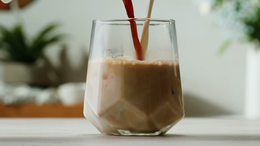 Ice coffee latte with cream being poured into it showing the texture and refreshing look of the drink, with a clean background.