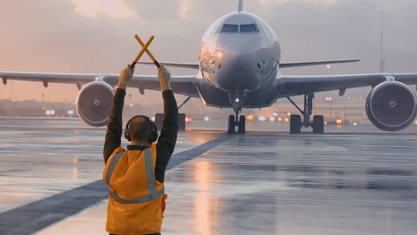 Ground Crew Member Guiding Commercial Aircraft On Wet Runway During Sunset Airport Operations