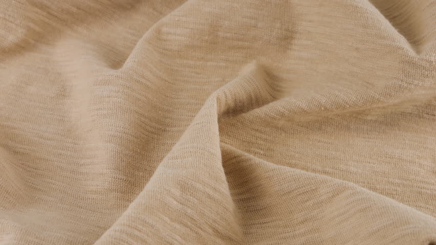 Top view of the soft folds of the thin beige cotton jersey. The textile background rotates on the display case. Background on the theme of fashion, design, natural fabrics.