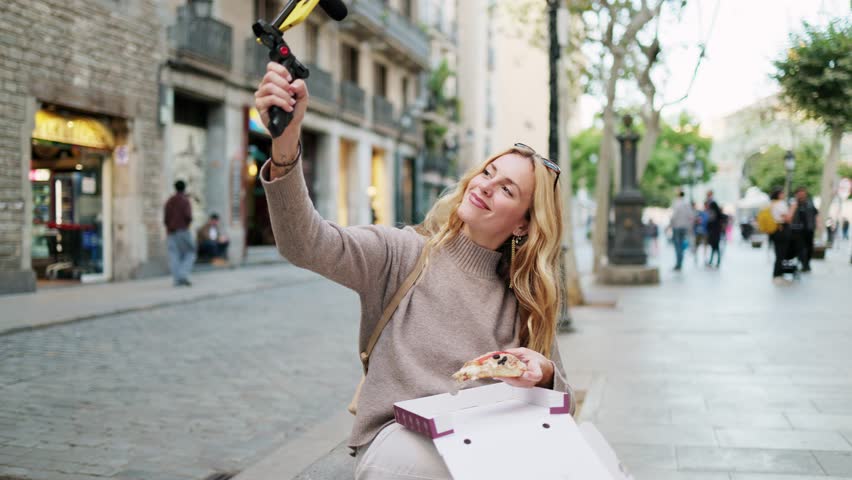 Travel influencer savors a slice of pizza while creating content for her vlog on a bustling city street.  Influencer enjoying pizza while vlogging on city street