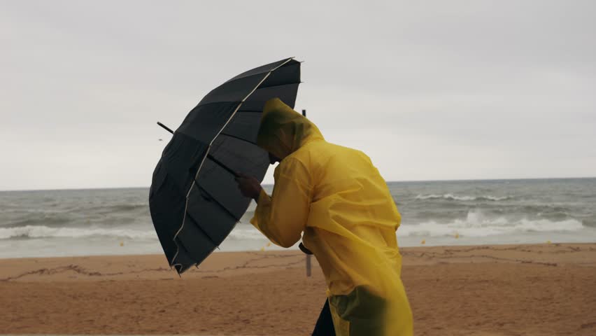 Man tourist person with umbrella and raincoat near sea ocean beach with storm on rainy european city street, lights reflecting, walking in Barcelona or Amsterdam during the rain.