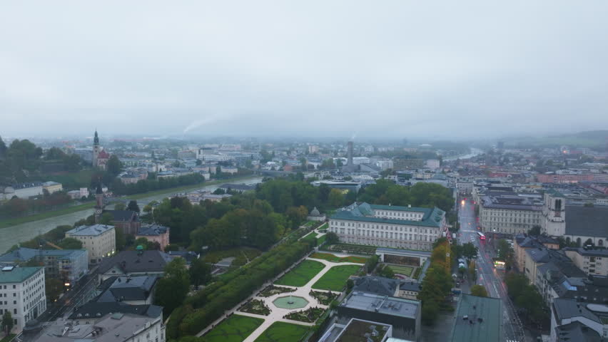 Aerial view of Salzburg, Austria featuring the gardens of Mirabell Palace and the Salzach River flowing through the city on a cloudy day