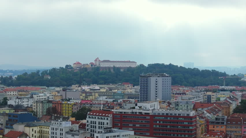 Birds are flying over the Brno skyline on a cloudy summer day. Spilberk castle, a 13th century fortress, is visible on the horizon on a hilltop