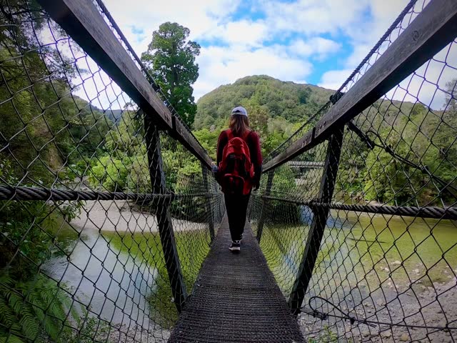 A lady walking on the suspension bridge over the river into the forest 