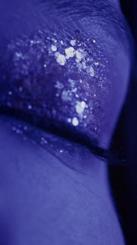 Portrait of a close-up opening eyes of a beautiful girl in a slow motion. Attractive millennial woman in the studio, neon blue pink light. Professional female model. Beauty fashion with glitter