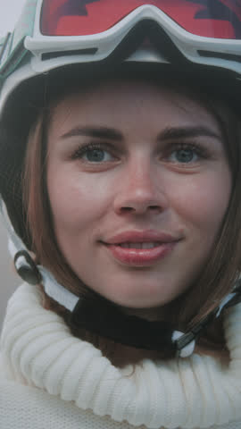 A beautiful Caucasian girl puts a white ski or snowboard helmet on her head. Portrait of a pretty woman at a winter resort. The female wears an orange protective mask or red glasses over her eyes.