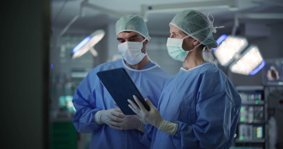 Before Beginning the Surgery, Female Lead Surgeon and an Assistant Looking at Detailed Brain Scans on a Large Computer Screen and a Tablet, Making Key Decisions Together with the Team