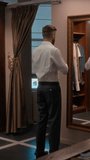 Vertical shot of man trying on stylish formal suit with help of sales assistant, examining his reflection in mirror while visiting menswear shop - Powered by Shutterstock - Get 15% off with code: PIKWIZARD15