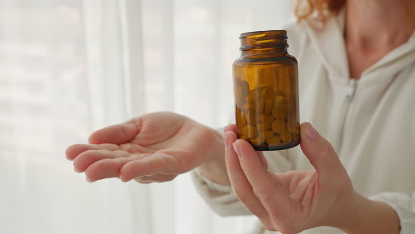 Close-up woman hands pouring white pills from brown bottle. Suggests healthcare, medicine, or supplements, highlighting daily wellness routines and personal health care. Vitamins for women's health